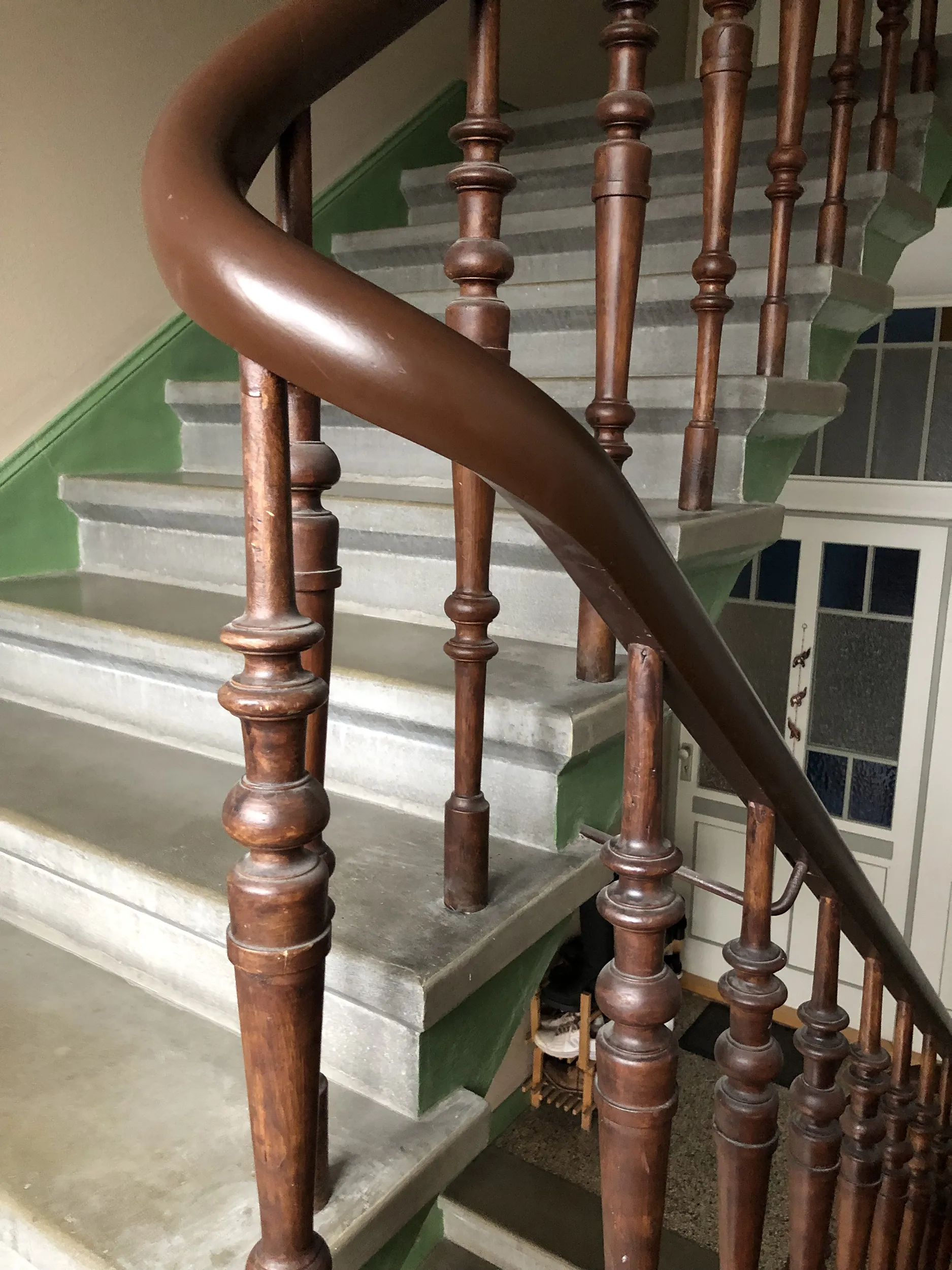 Holzgeländer und -balustraden auf einer mit grünen und grauen Motiven verzierten Treppe, die von unten an der Kurve sichtbar ist.