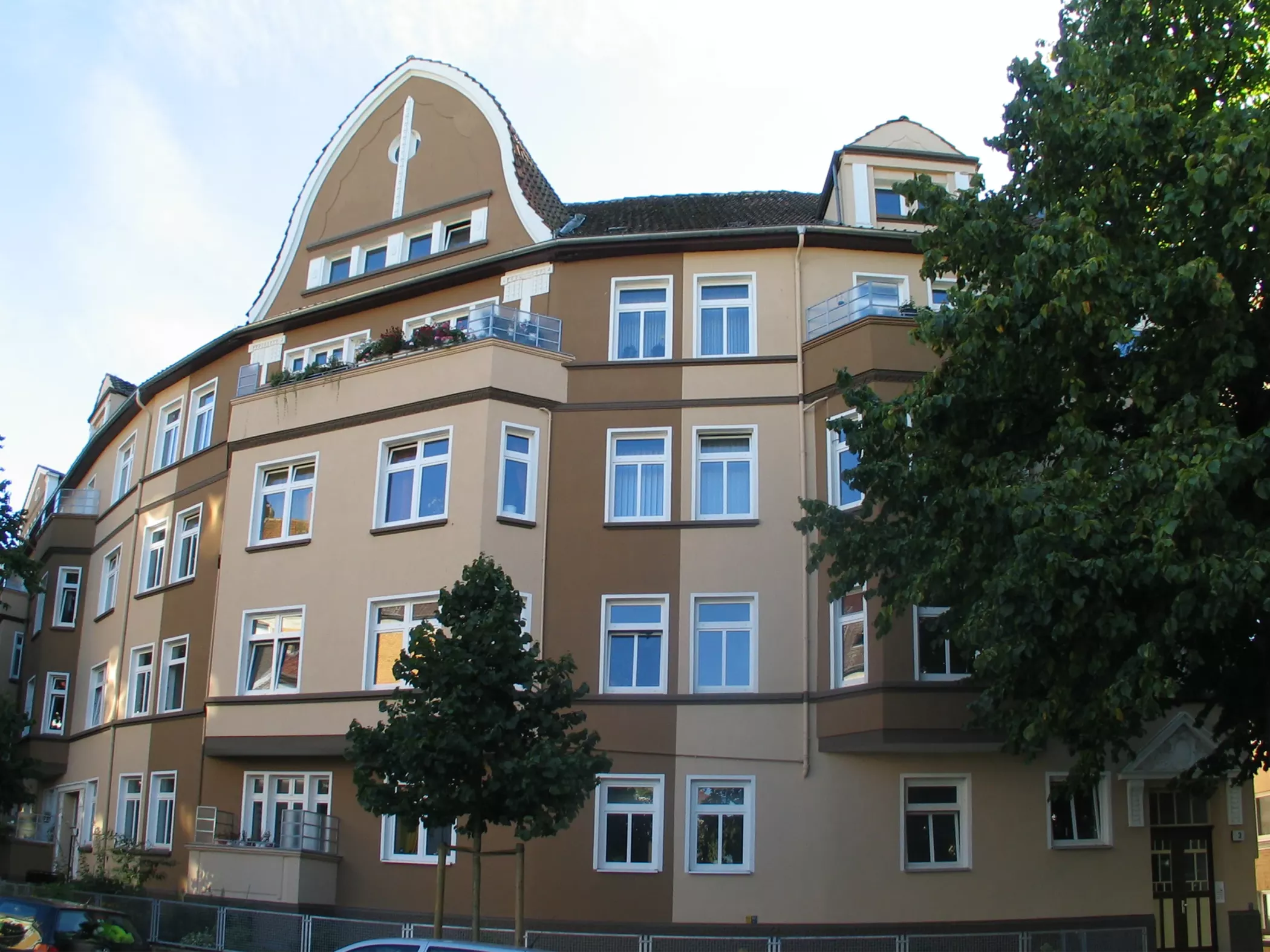 Ein großes braun-beigefarbenes Wohnhaus mit weiß verzierten Fenstern und einem Baum auf der Vorderseite.