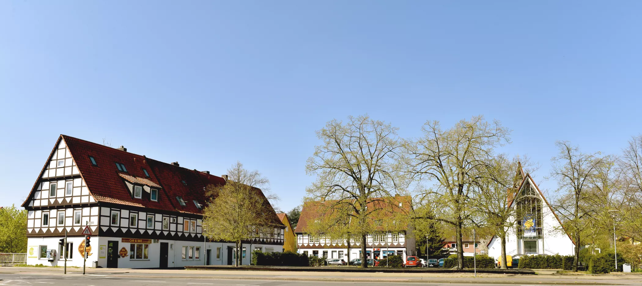 Traditionelle Fachwerkhäuser mit roten Dächern und Bäume unter einem klaren blauen Himmel an einem sonnigen Tag.