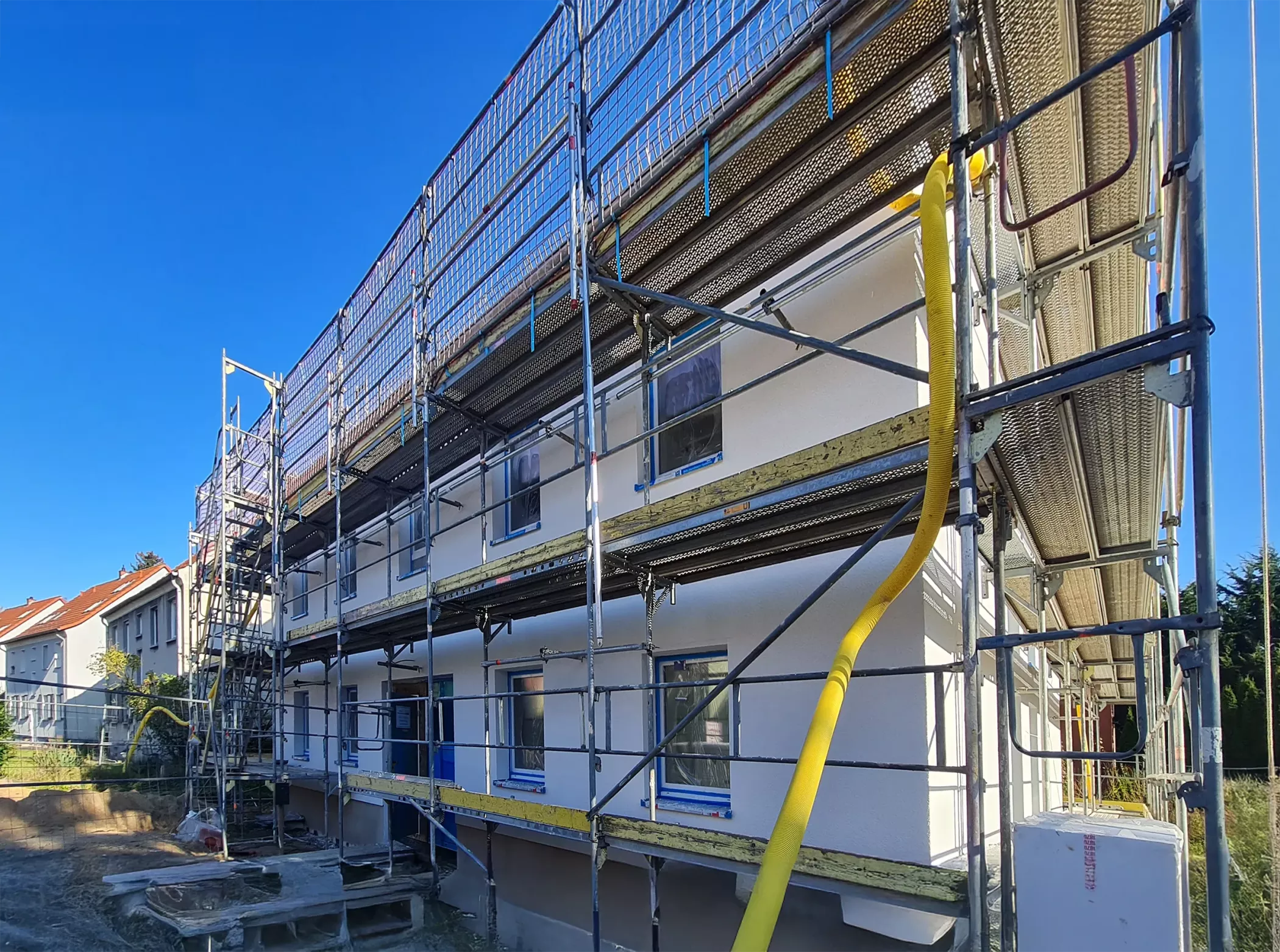 İnşaat halinde, iskele ve güvenlik ağlarıyla kaplı beyaz bir bina ve iki sarı kaydırak.