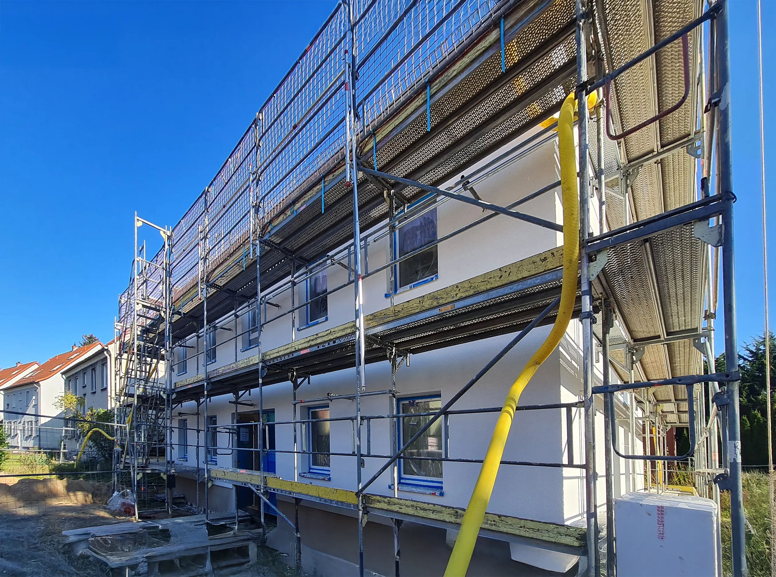 İnşaat halinde, iskele ve güvenlik ağlarıyla kaplı beyaz bir bina ve iki sarı kaydırak.