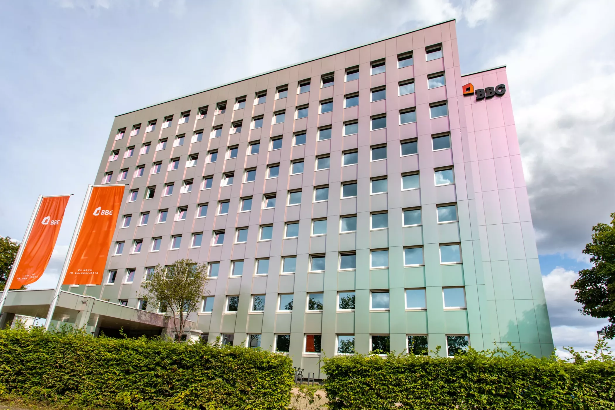 Ein modernes, mehrstöckiges Bürogebäude mit vielen Fenstern, orangefarbenen ABB-Fahnen und einem Zaun an der Vorderseite, unter einem teilweise bewölkten Himmel.