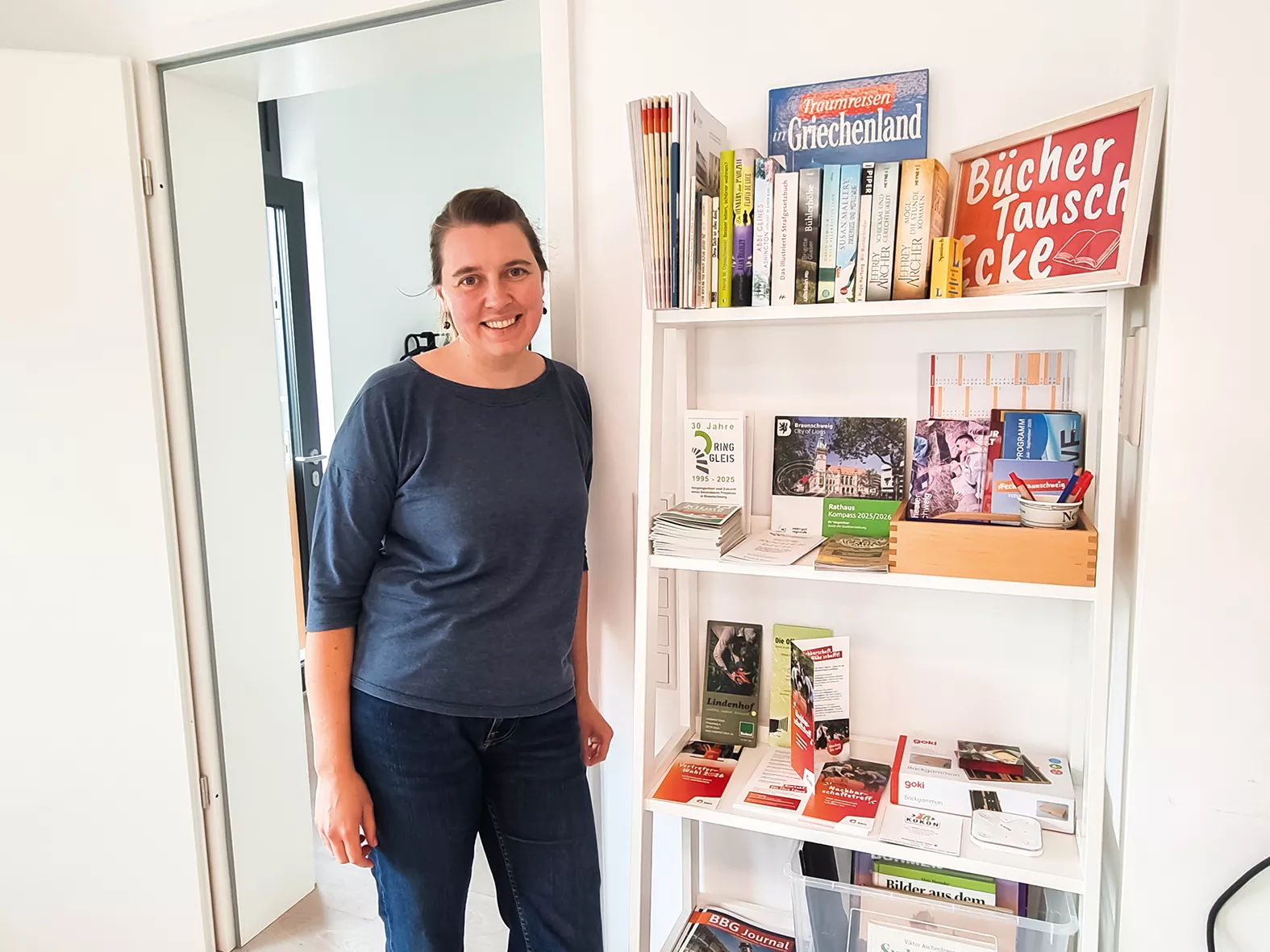 Eine Frau steht neben einem Regal voller Bücher, Zeitschriften und Broschüren in einem hell beleuchteten Raum.