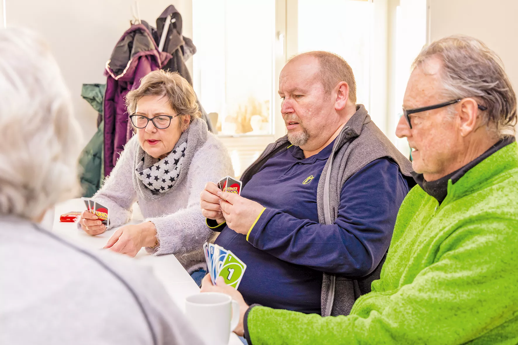 Vier ältere Menschen sitzen um einen Tisch herum und spielen gemeinsam ein Kartenspiel; sie konzentrieren sich auf ihre Karten.