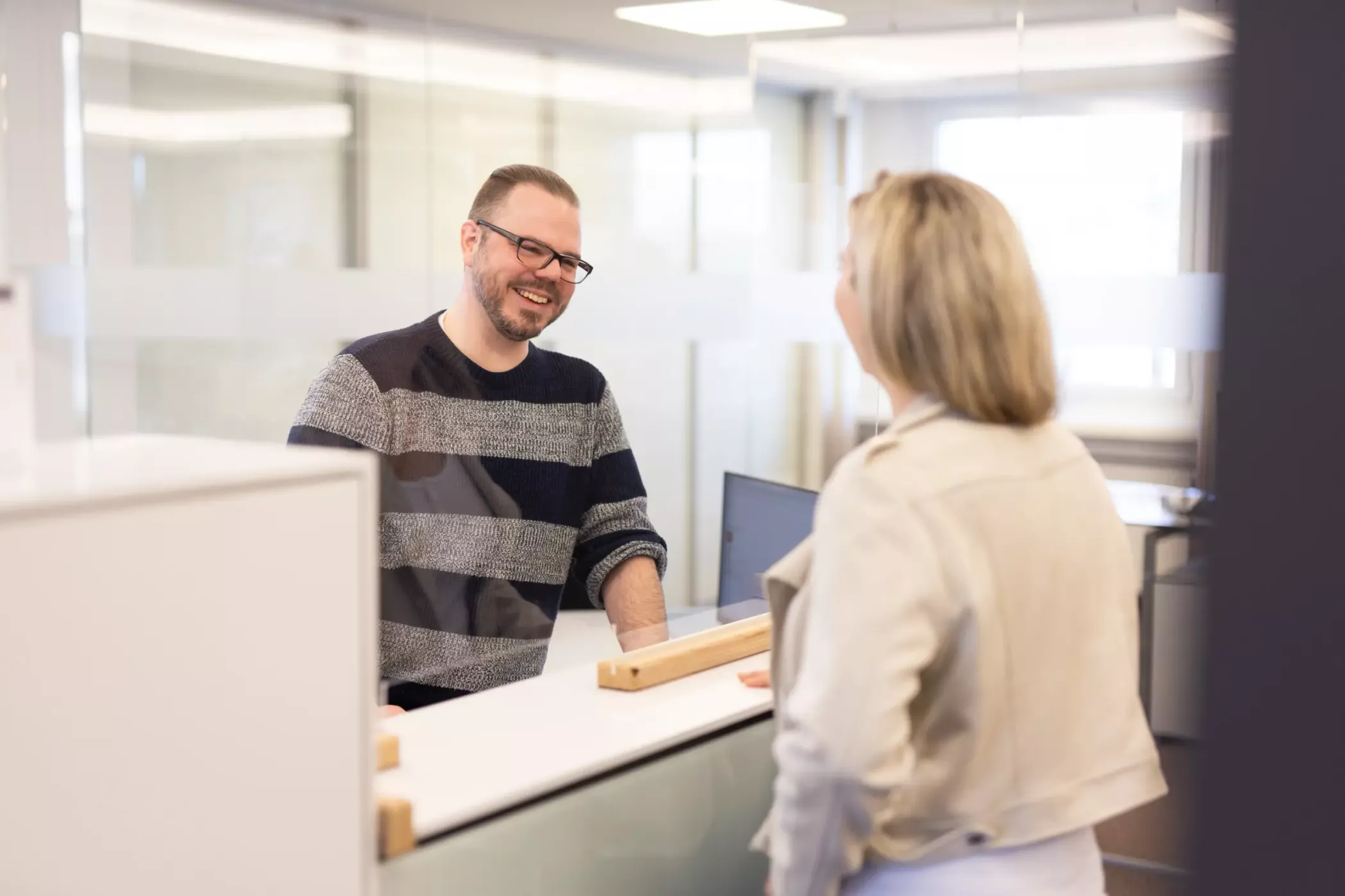 رجل وامرأة يتحدثان في مكتب استقبال في مكتب حديث ومشرق. الرجل يبتسم.