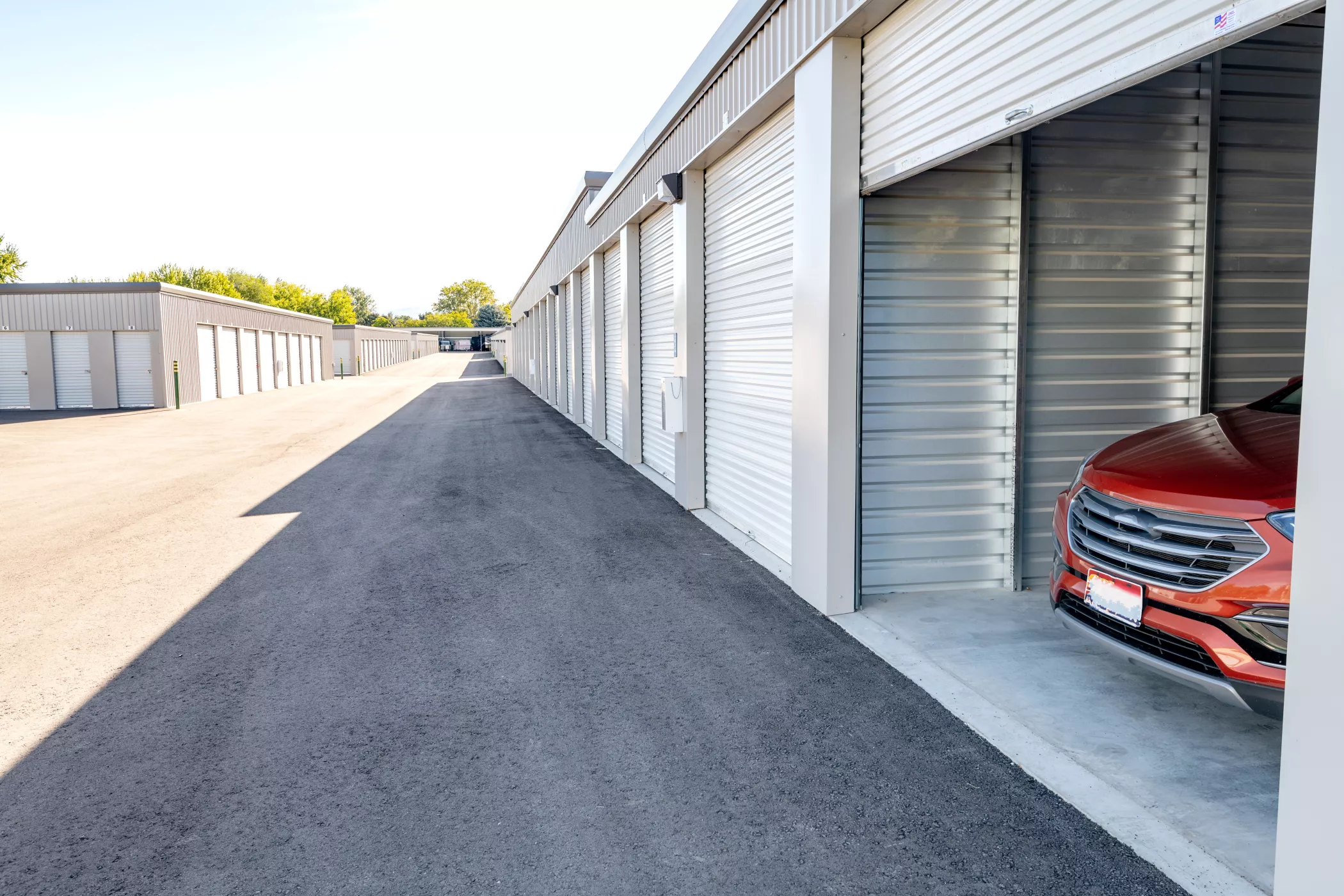 Eine Reihe von Lagerhäusern mit einem offenen Lagerhaus, in dem an einem sonnigen Tag ein roter Geländewagen geparkt ist.
