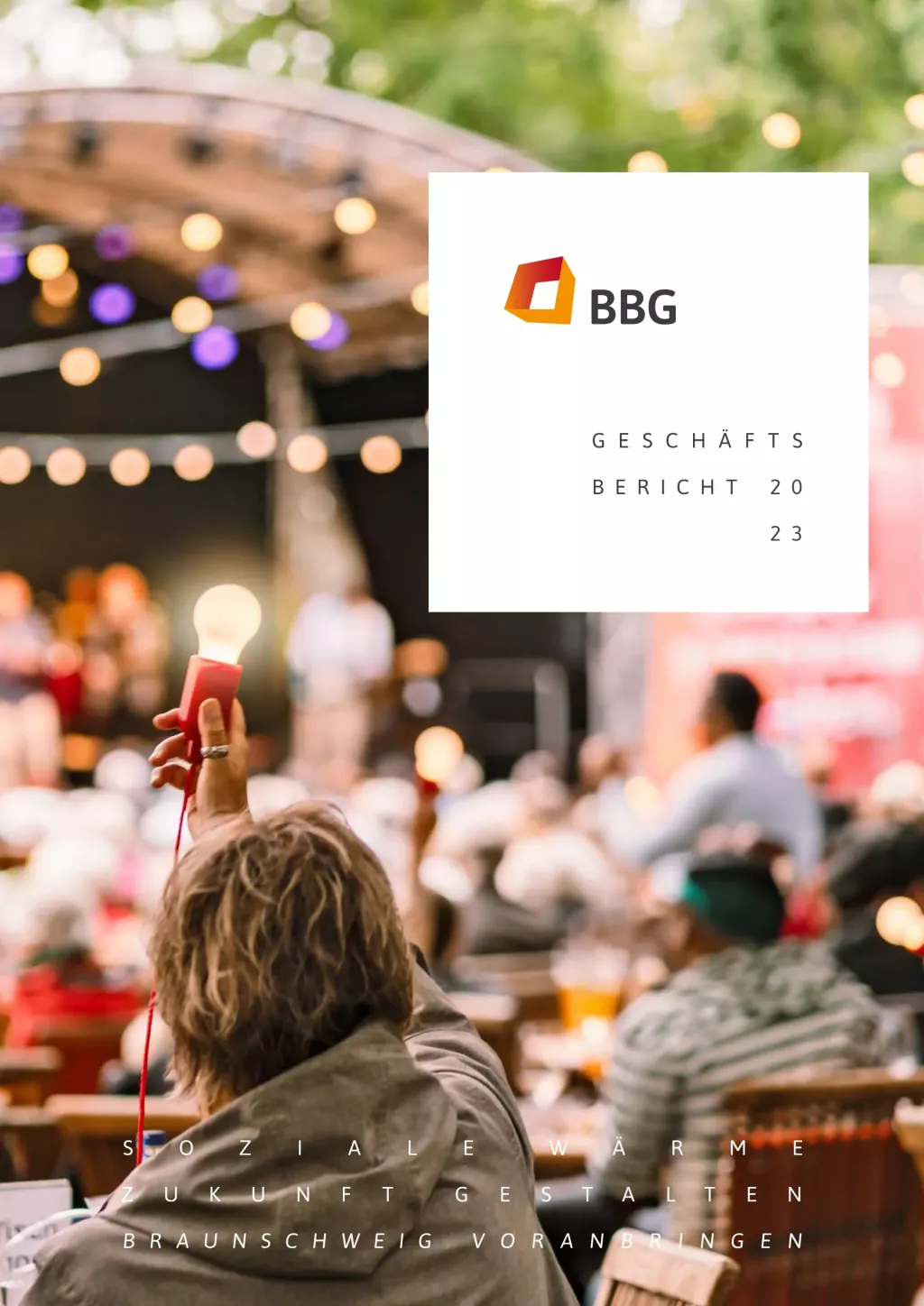 Eine Person hält eine Fackel bei einer Veranstaltung im Freien mit unscharfen Menschen und einem Theater im Hintergrund. Textüberlagerungen mit der Aufschrift 