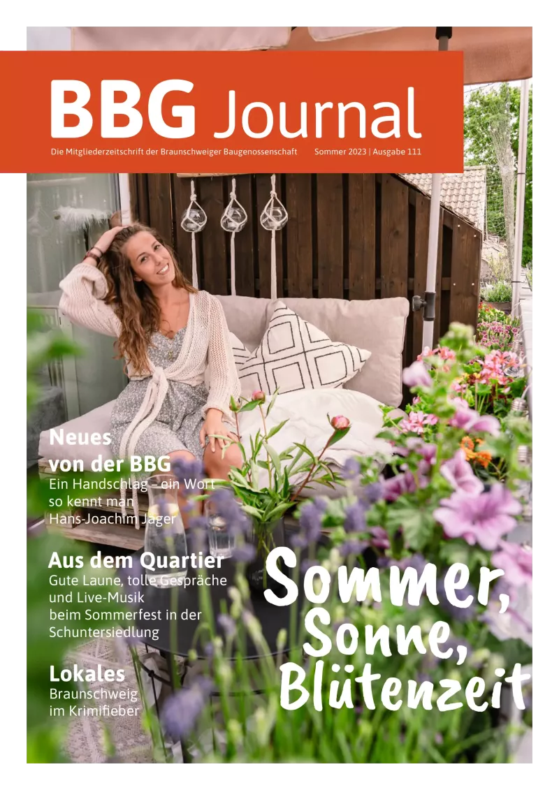 Eine lächelnde Frau in einem weißen Kleid sitzt auf einem gemütlichen Sofa im Freien, umgeben von Kissen und Pflanzen, mit einem Text-Overlay aus einer Sommerzeitschrift.