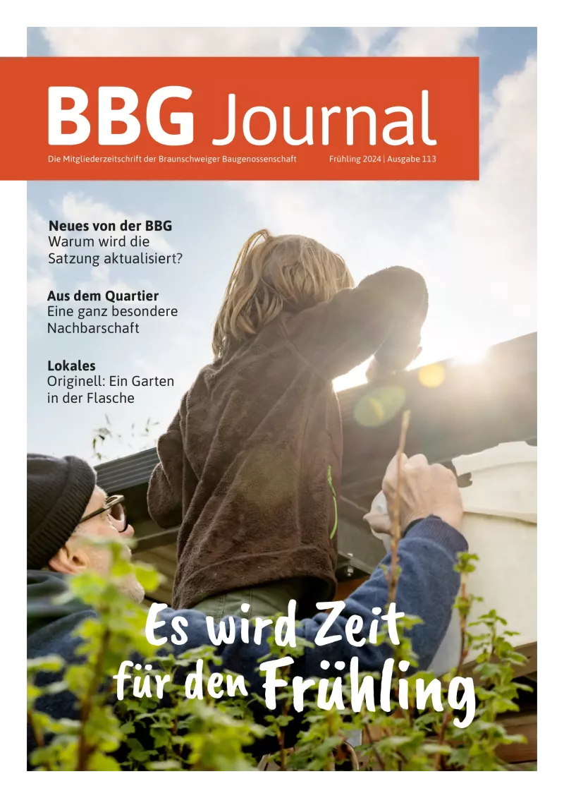 Ein Kind auf der Schulter eines Erwachsenen streckt sich der Sonne entgegen, die Menschen um es herum lächeln unter einem klaren Himmel.