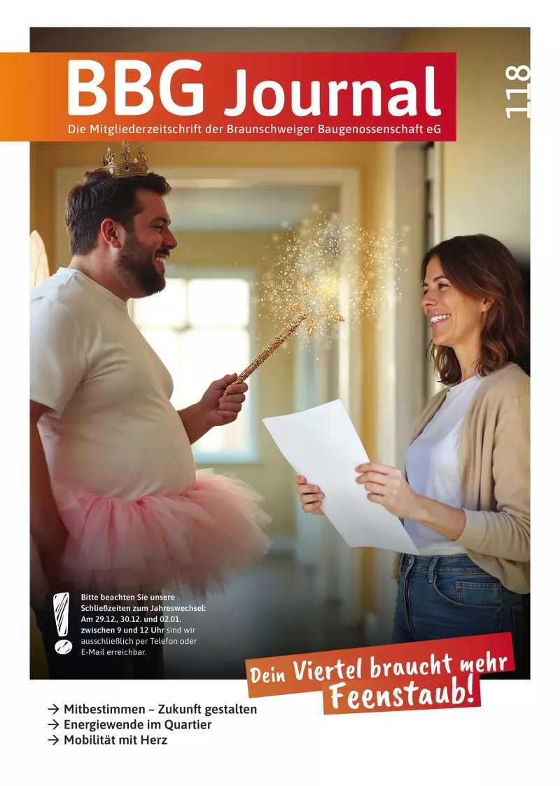 Ein lächelnder, als Fee verkleideter Mann überreicht einer Frau, die ein Klemmbrett in der Hand hält, ein Dokument, beide sehen glücklich und freundlich aus.