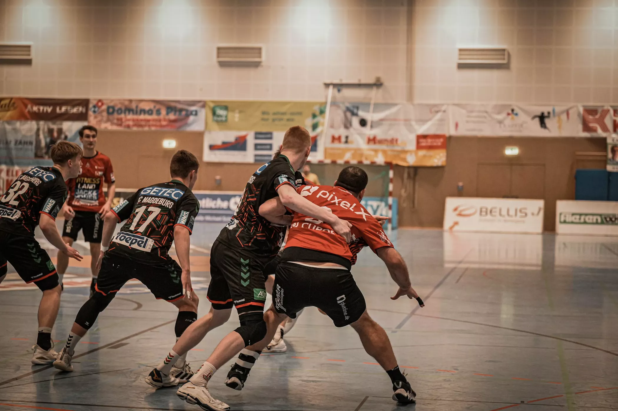Handball players in action on a closed court, with one player trying to block another player during the game.