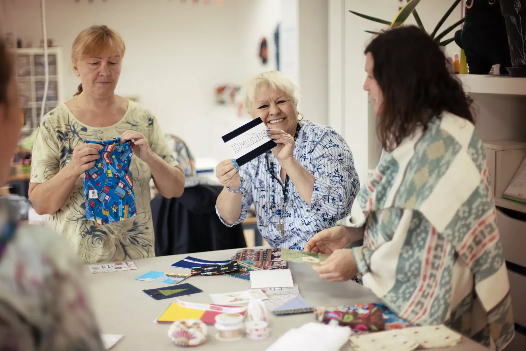 Three people enjoying a craft activity together at a table, smiling and showing a canvas and a card labeled Dunk.