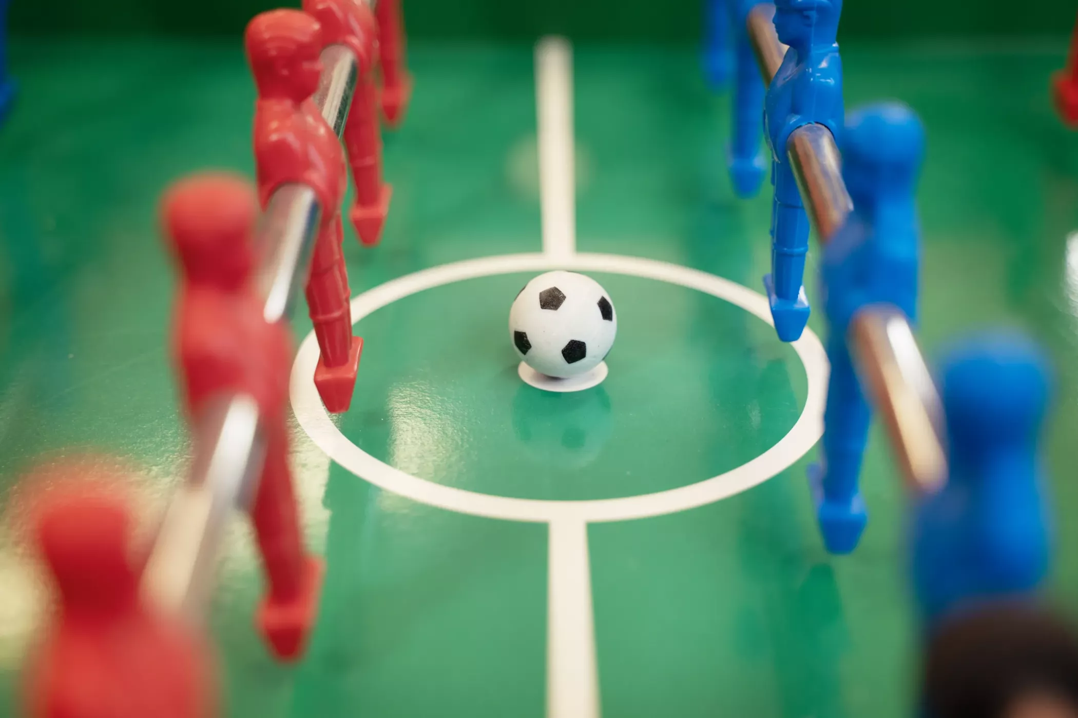 Eine Nahaufnahme eines Fußballtisches mit roten und blauen Spielern und einem schwarz-weißen Fußball im Mittelkreis.
