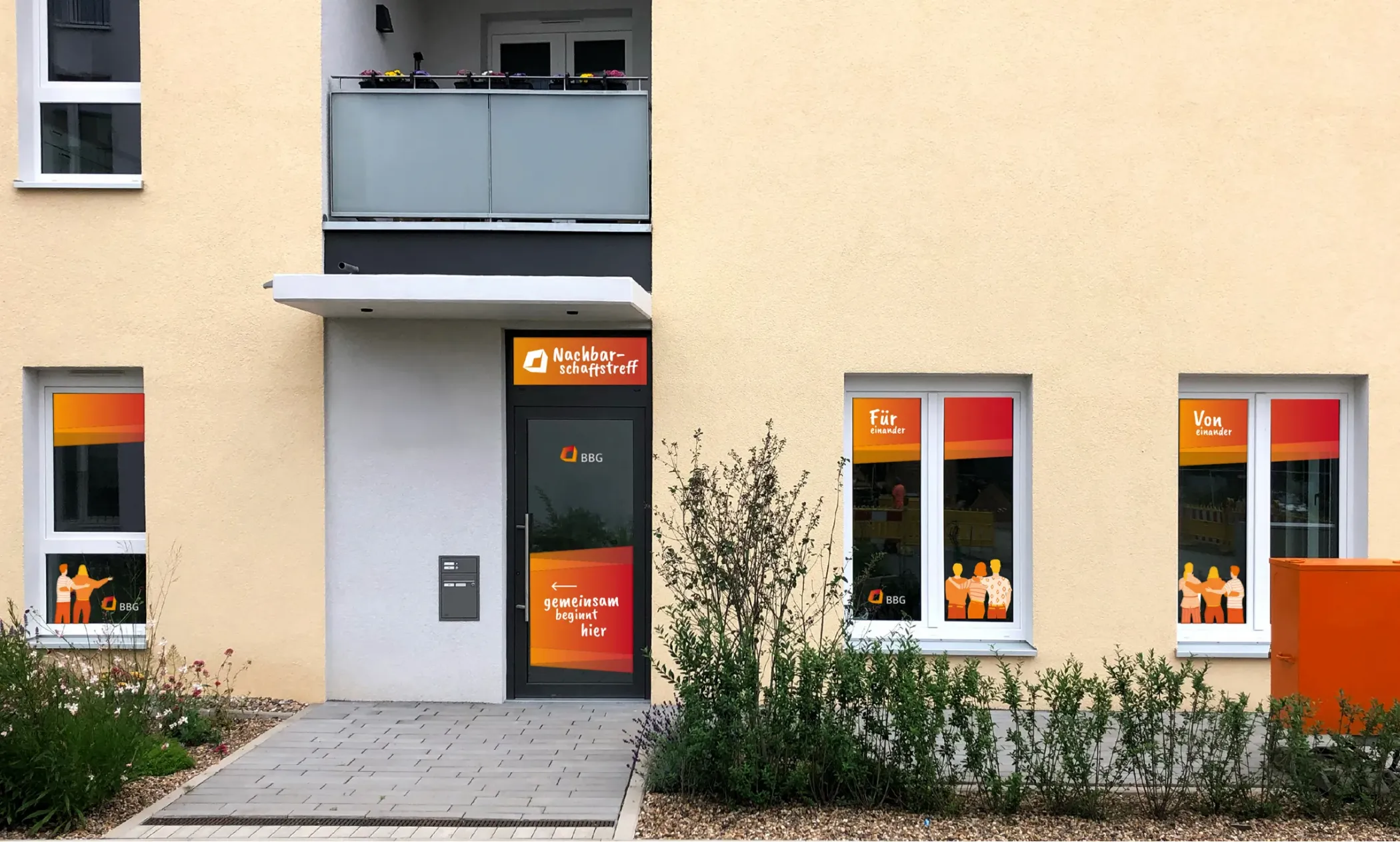 Entrance to a community center with orange, yellow and red banners on the windows, doors and balconies of the apartments above.