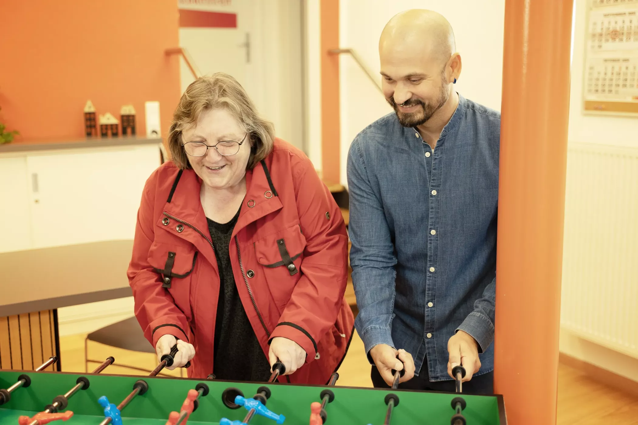 Eine ältere Frau und ein Mann lächeln, während sie in einem Haus Fußball spielen.