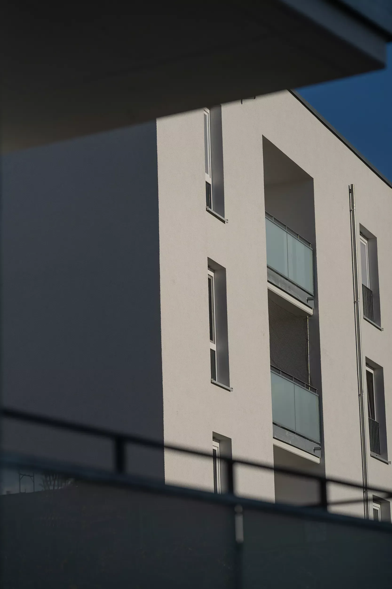 مبنى سكني أبيض عصري بشرفات زجاجية مظللة جزئياً ومظلل جزئياً أمام سماء زرقاء صافية.