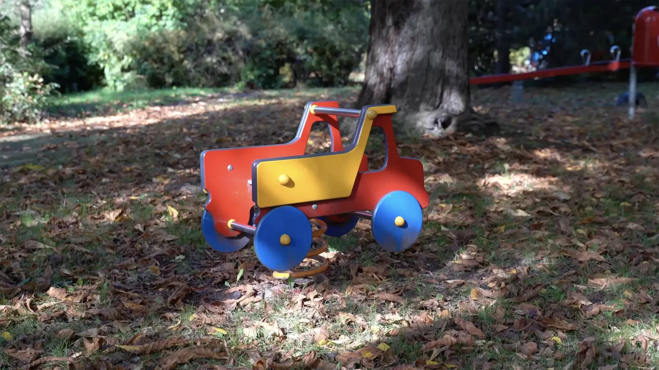 A colorful spring rider in the shape of a toy car sits on the green ground under the trees in the park.