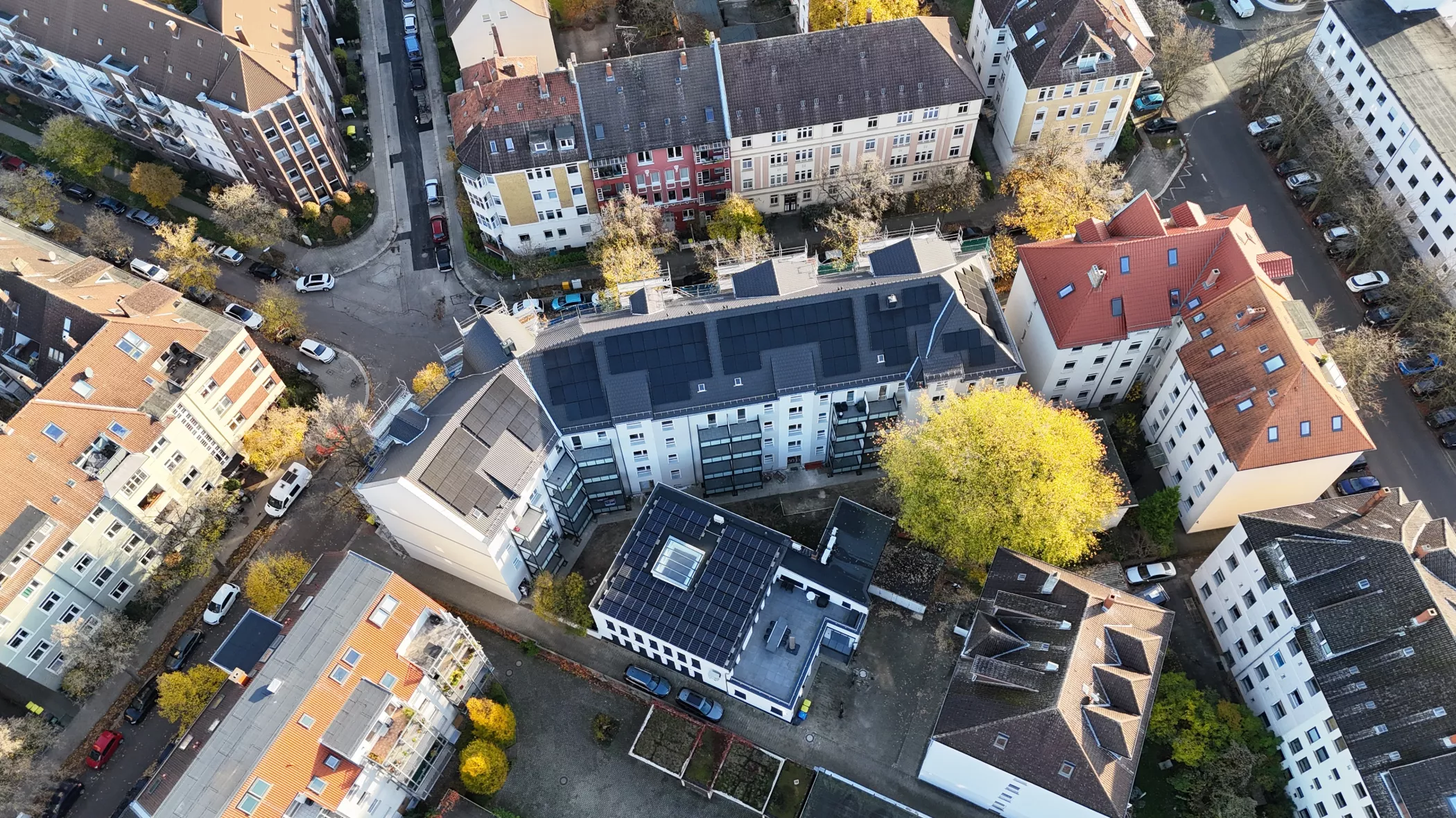 Eine Luftaufnahme von Wohngebäuden mit Sonnenkollektoren, umgeben von Bäumen und Straßen in einem städtischen Viertel.