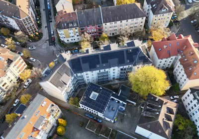 Eine Luftaufnahme von Wohngebäuden mit Sonnenkollektoren, umgeben von Bäumen und Straßen in einem städtischen Viertel.