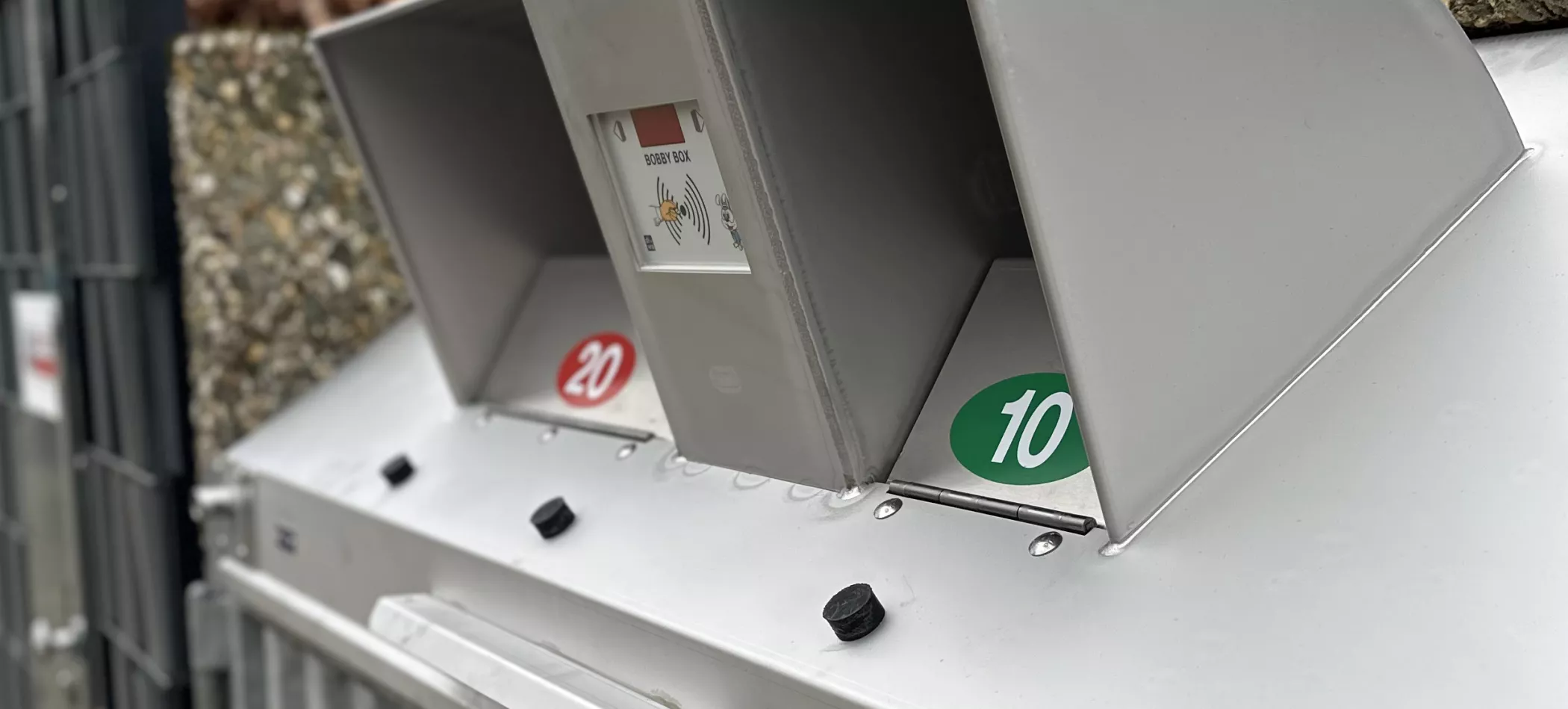 Nahaufnahme eines Metallautomaten, der Münzeinwurföffnungen zeigt, auf denen rote kreisförmige Markierungen mit dem Wert 20 und grüne mit dem Wert 10 zu sehen sind.