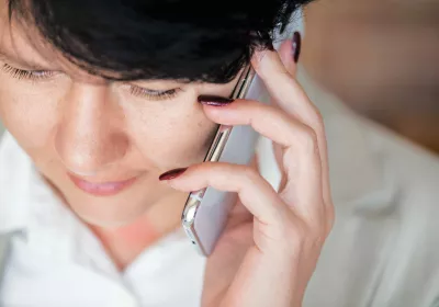 Nahaufnahme einer Person mit schwarzen Haaren, die ein Smartphone an ihr Ohr hält und telefoniert.