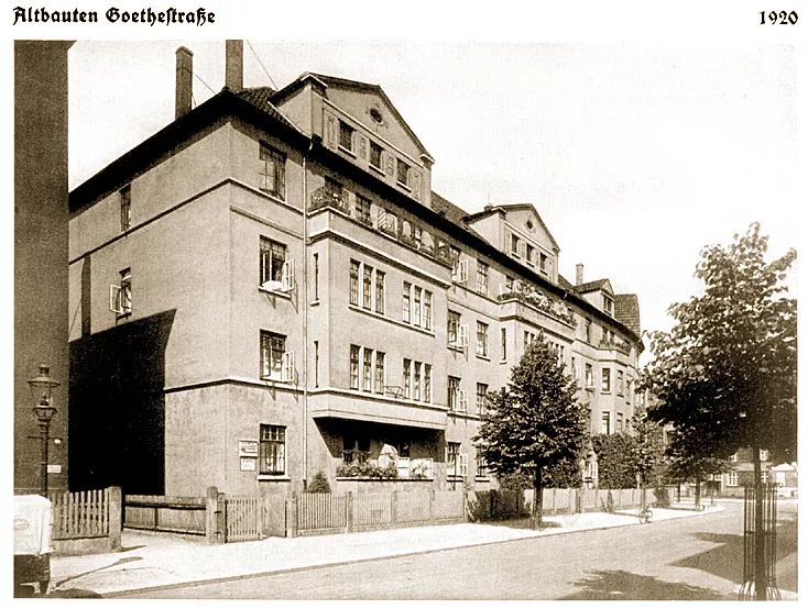 Photographie historique en noir et blanc de bâtiments à plusieurs étages dans la Götstraße avec des arbres et une clôture, datée de 1920.
