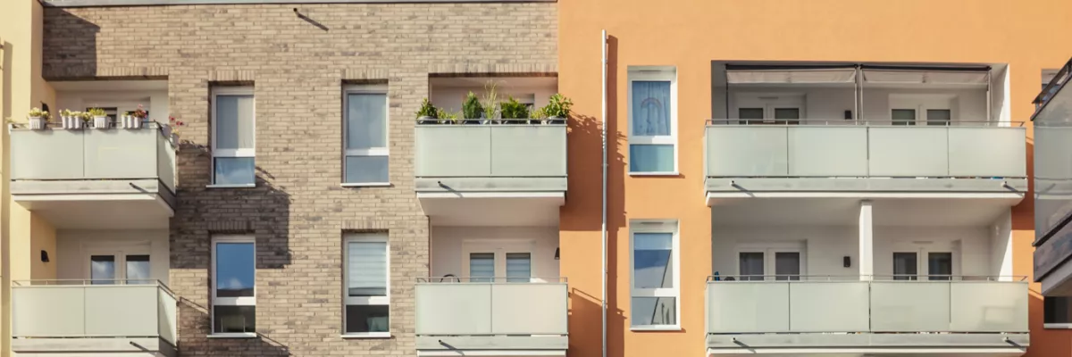 Ein modernes Wohngebäude mit Backstein- und Orangenfassaden, Balkonen, Glasgeländern und einigen Topfpflanzen.