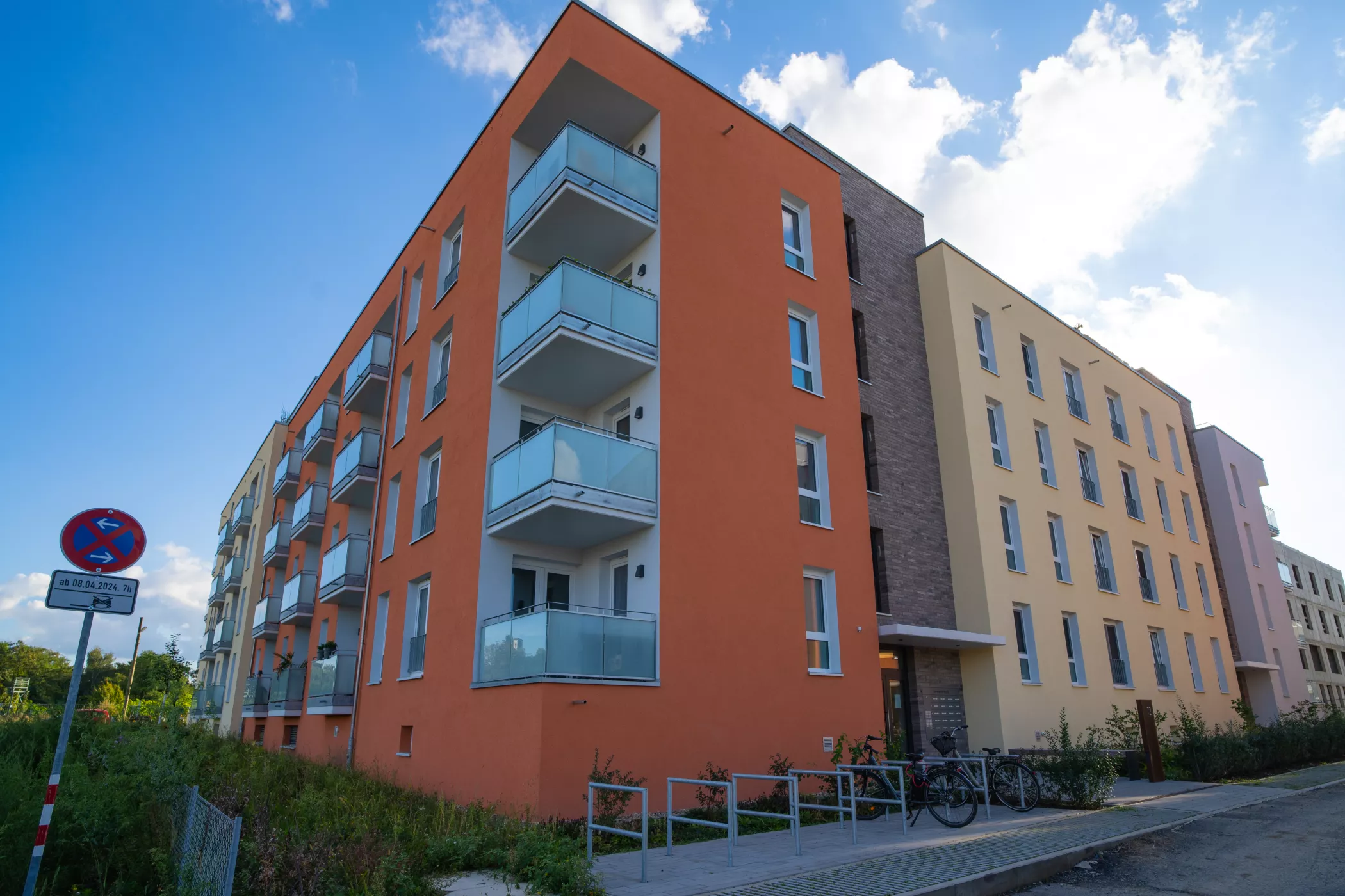 Turuncu ve sarı duvarları, balkonları ve üzerinde masmavi bir gökyüzü olan dört katlı modern bir konut binası.