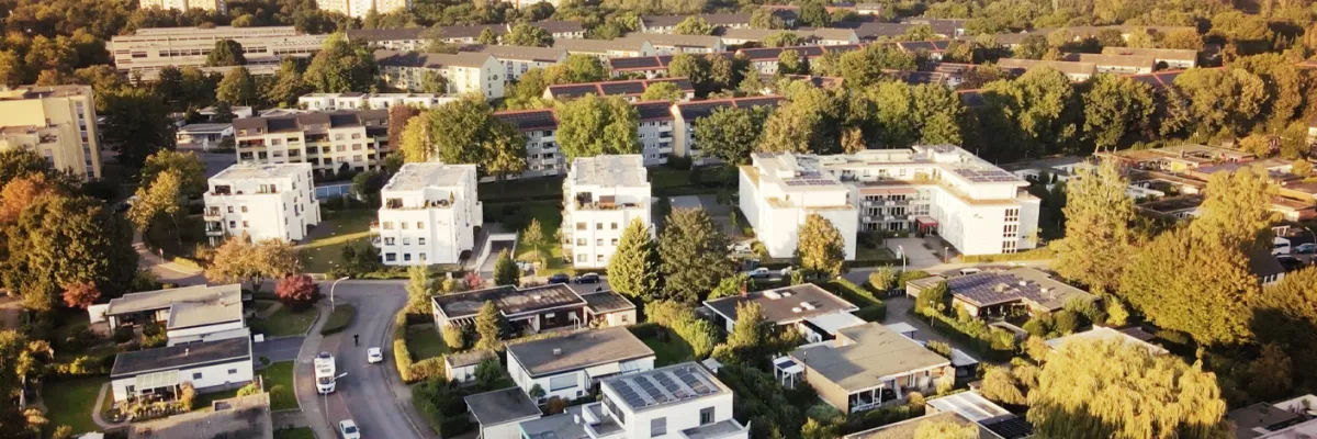 Eine Luftaufnahme eines Vorstadtviertels mit modernen Häusern, grünen Bäumen und verwinkelten Straßen an einem sonnigen Tag.