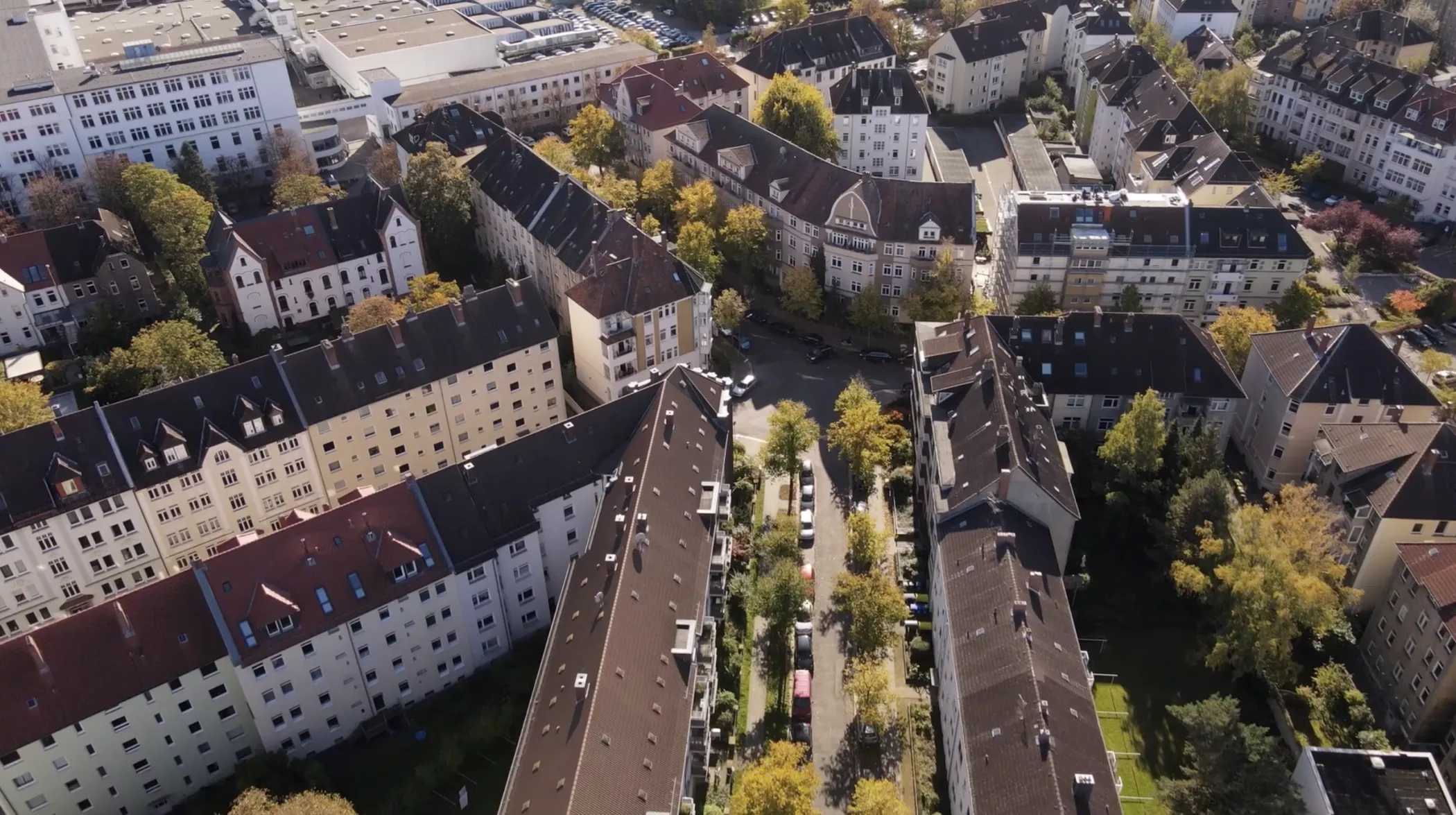 An aerial view of residential buildings with pitched roofs and tree-lined streets in a neighborhood on a sunny day.