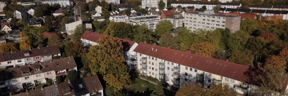 Luftaufnahme eines Wohngebiets mit Wohngebäuden, Häusern und Bäumen unter einem klaren blauen Himmel.