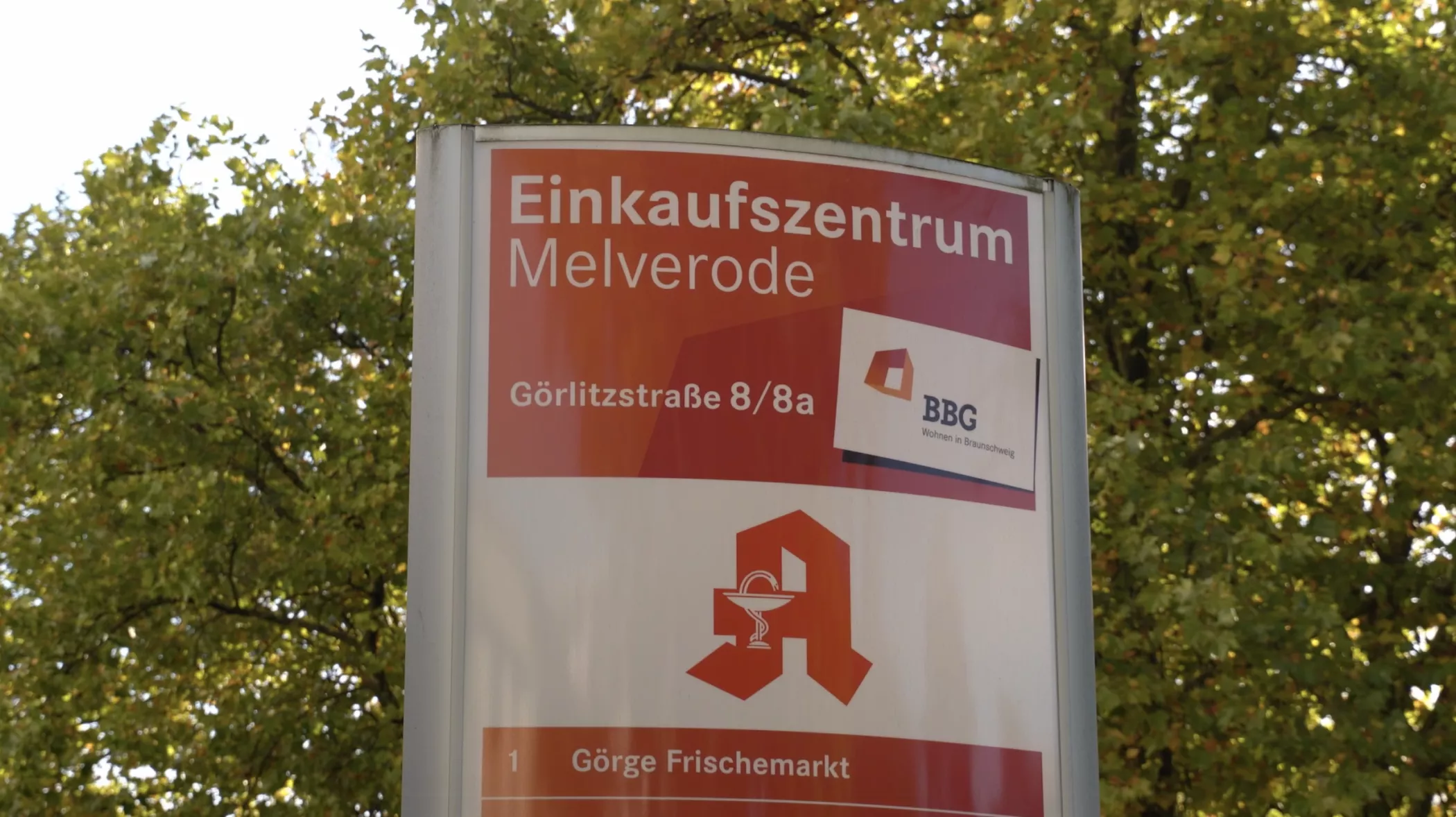 Schild für das Einkaufszentrum Melverode, mit der Adresse Görlitzstraße 8/8a, mit einer Apotheke und einem Logo im Hintergrund.