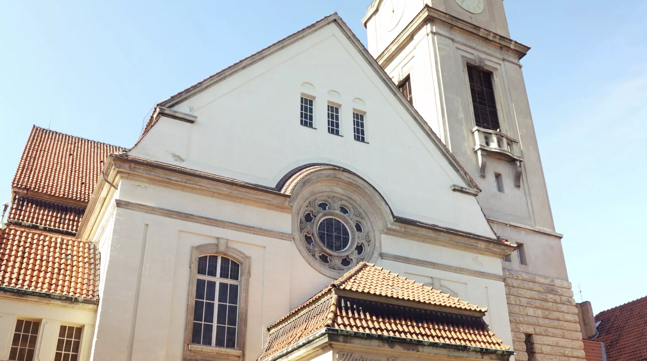 Eine weiße Kirche mit Ziegeldach, gewölbten Fenstern und einem hohen Glockenturm vor einem strahlend blauen Himmel.