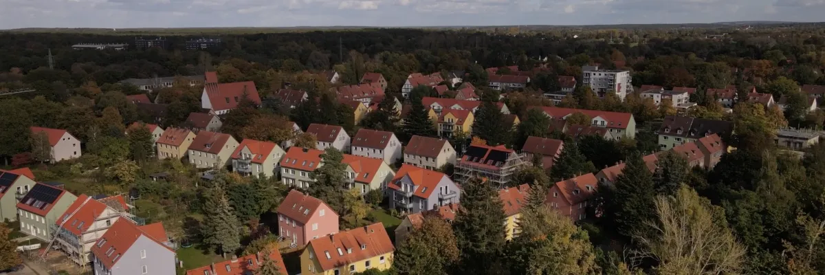 Aerial view of a suburban neighborhood with red-roofed houses surrounded by trees under a partly cloudy sky.