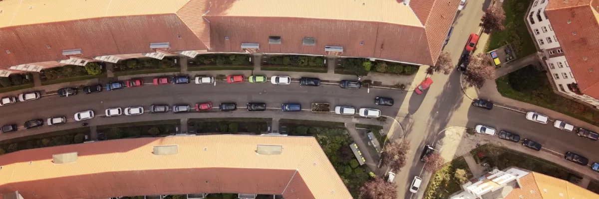 Eine Luftaufnahme von geschwungenen Wohnhäusern mit roten Dächern, parkenden Autos und grünen Bäumen entlang der Straße.