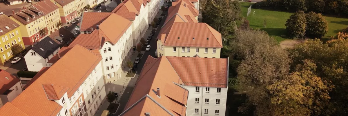 Eine Luftaufnahme von Wohngebäuden mit roten Dächern, baumbestandenen Straßen und einem grünen Park auf der rechten Seite.
