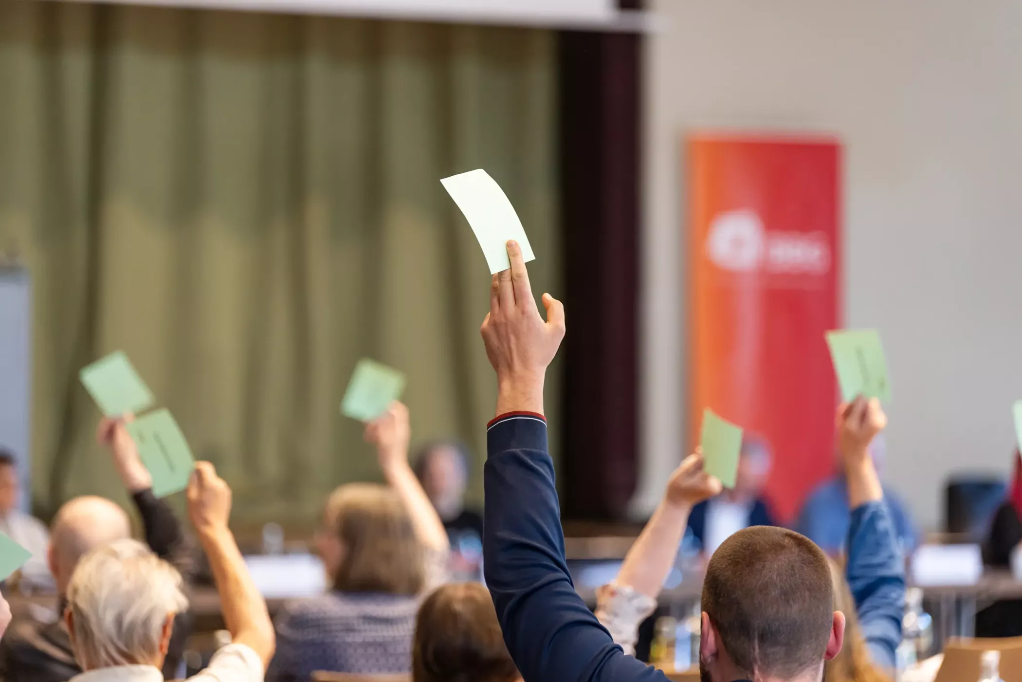 Menschen, die bei einer Sitzung oder Konferenz eine grüne Karte hochhalten, um abzustimmen oder an einer Gruppenentscheidung teilzunehmen.