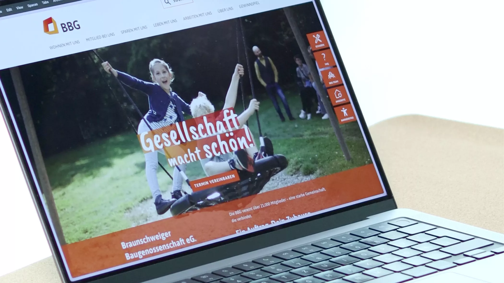 Ein Laptop zeigt eine Website an, auf der Kinder auf einer Schaukel spielen und ein deutscher Text auf dem Bildschirm eingeblendet ist.