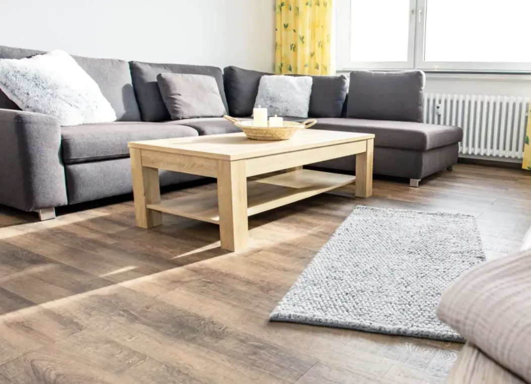 A bright living room with a gray sectional sofa, a light wood coffee table and a gray rug on a wooden floor.